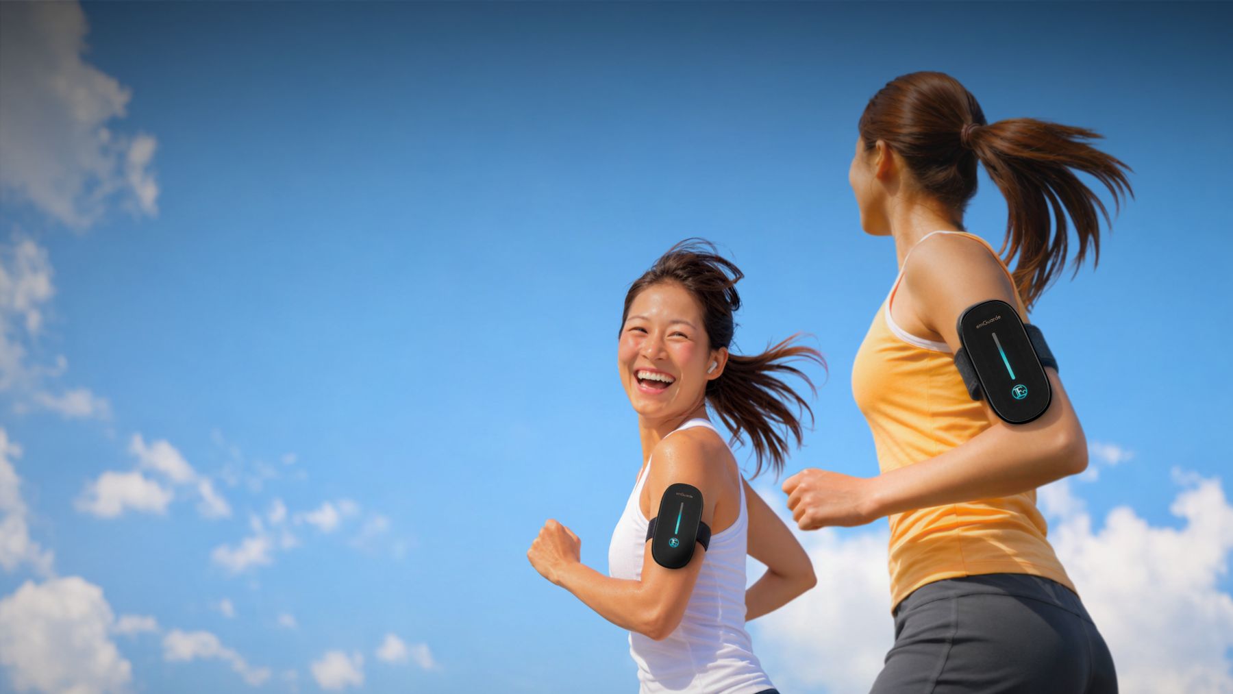 Two women running outdoors wearing emGuarde in armbands